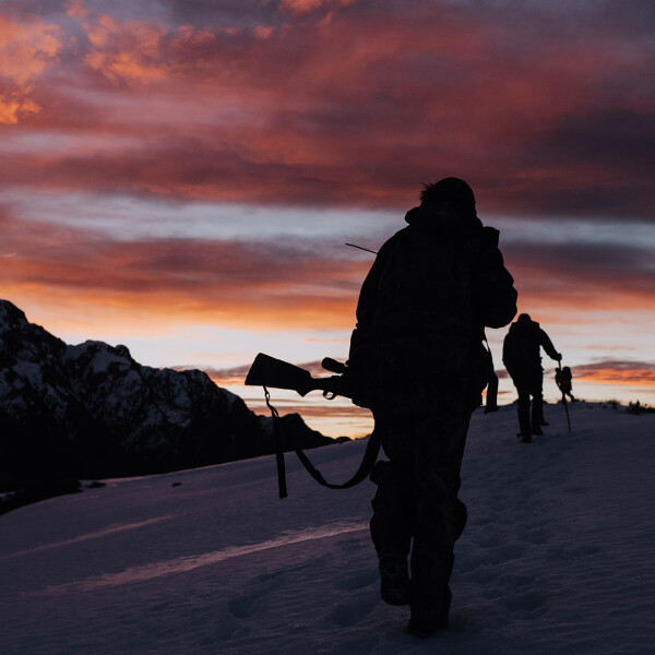 Alpine hunters tramping snow at dusk